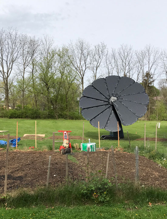 SmartFlower solar panel blooming beside fenced vegetable garden with tools and compost materials visible