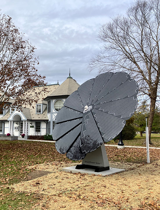 SmartFlower solar panel positioned in front of historic white building with autumn leaves
