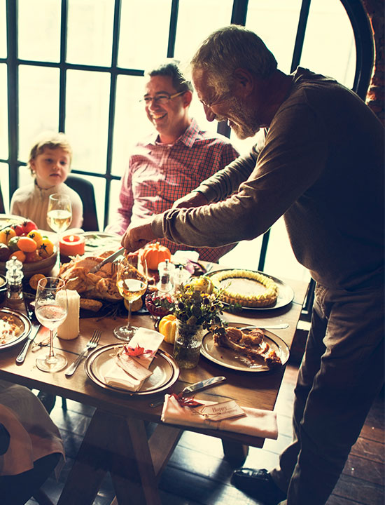 Man carving roasted turkey while others smile during cozy holiday meal celebration