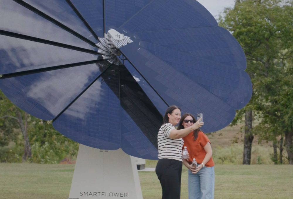 Two woman are taking a picture in front of a SmartFlower that is installed at Henderson Innovation Park in Henderson, Texas