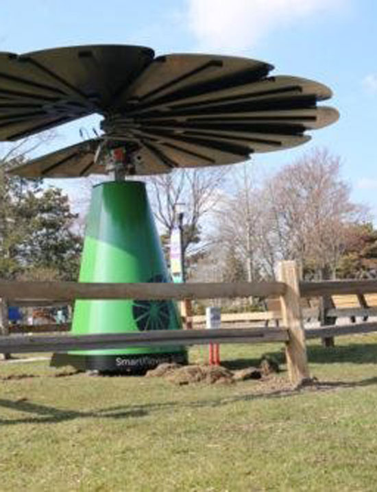 A SmartFlower solar panel system partially closed, located in a fenced grassy area
