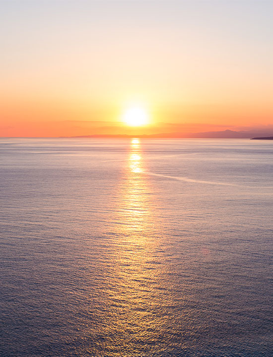 Peaceful seascape at sunset showing warm sky hues mirrored on gentle ocean surface