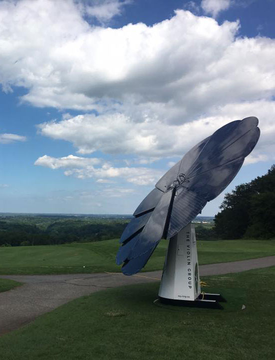 Large solar panel displayed on grassy hilltop under a partly cloudy blue sky