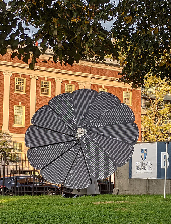 Photovoltaic SmartFlower unit beside BFIT sign and historic brick academic building